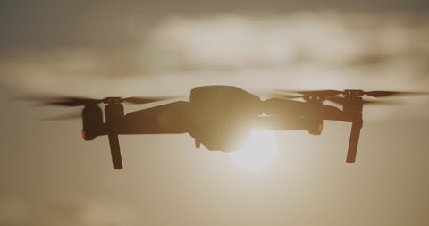 Silhouette of drone flies against bright sky in evening or morning. Modern technologies for shooting photos and videos from above. Sunset, sunrise, golden hour. Drone backlit in sunshine