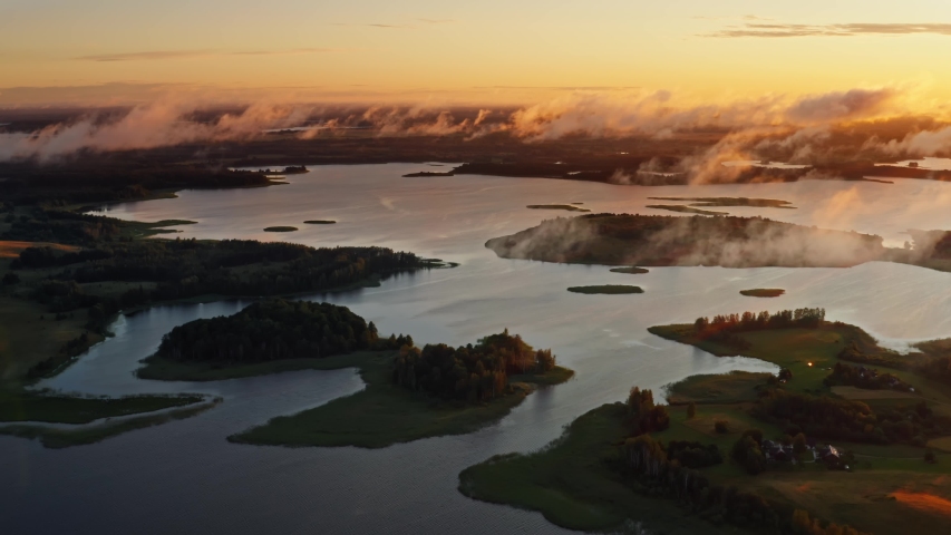 Amazing lake land view from above, drone flies over beautiful islands and moving clouds in morning sunlight. Aerial, flight over lakes during fantastic sunrise. Colorful warm skyline on horizon
