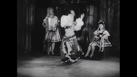 CIRCA 1940s - Burlesque performer Deena Newell finishes a dance with a tambourine in a revealing Romani costume while two women play accordion.