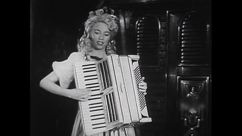CIRCA 1940s - Burlesque performer Deena Newell dances and plays the tambourine in a revealing Romani costume while two women play accordion.