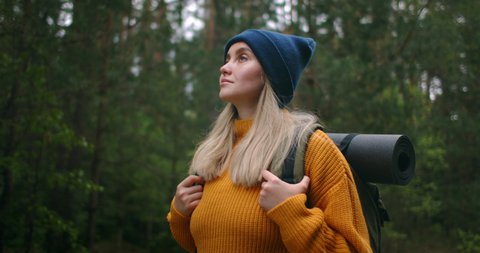 Portrait low angle a woman with a backpack in a yellow sweater and hat is walking along a road in the woods in slow motion.