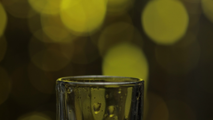 Bartender pouring up frozen vodka from bottle into shot glass against shiny gold party celebration background. Barman pour of cold transparent alcohol drink vodka tequila in shot-glass Royalty-Free Stock Footage #1056880430