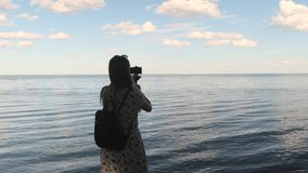 Rear view portrait of a woman making a video of a beautiful sea landscape with smartphone and monopod at sunset