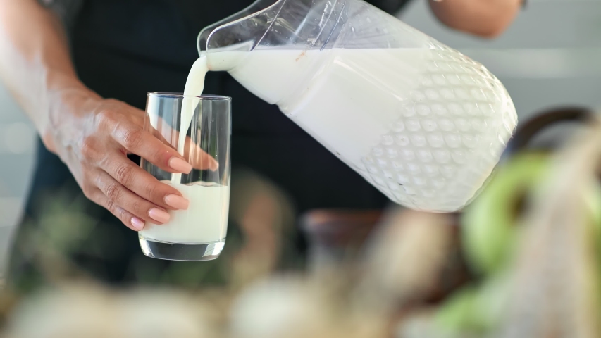 Closeup female hands pouring fresh homemade milk from jug into glass. Agricultural woman filling transparent glassware by liquid eco beverage. Royalty-Free Stock Footage #1056881390