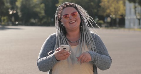 Happy very stylish expressive attractive obese woman with afro braids listening to music through headphones and moving to the beat