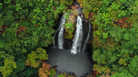 Drone moves away from a mountain waterfall in an autumn forest (Opaekaa Falls, Kauai, Hawaii, USA)