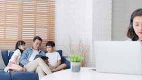 Young Asian mother work at home with family, father, daughter, and son sit together on sofa couch. New normal lifestyle, remote video call online conference meeting concept