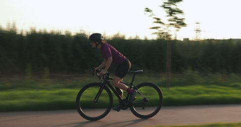 Female pro cyclist is hard pedaling on road aero bike at sunset. Woman athlete is training on bicycle and preparing for competition race. Professional triathlete is cycling at sunset. Cycling concept