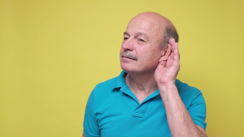 Senior man trying to listen to the latest news holding hand near ear. Studio shot. | Shutterstock HD Video #1056889772