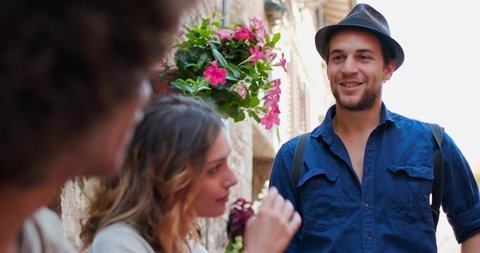Three tourists talking, smiling, and having fun near a brick wall in rural town of Spello. Man taking off his hat. Group of happy people talking outdoor. Friends italian trip in Umbria.4k slow motion