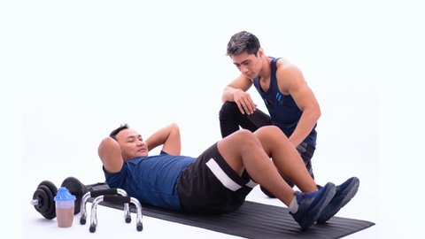 trainer accompanies a man doing sit up exercises holding back to make the right moves with mat on an isolated background