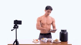man health and sports blogger showing healthy food menu while holding egg and tablet stand facing forward and look to recording camera on isolated background