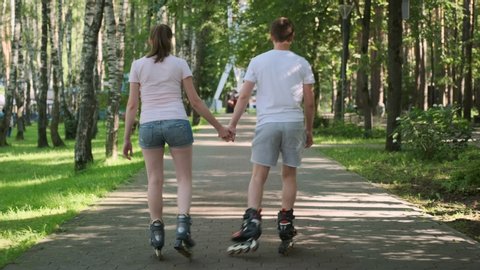 Couple in love to roller skate down alley in park on sunny summer day.