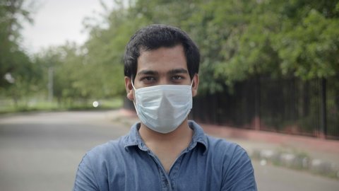 A close shot of a happy young man male standing outdoors removes the face protective mask and smiles looking at the camera lens amid Corona virus COVID 19 epidemic or pandemic