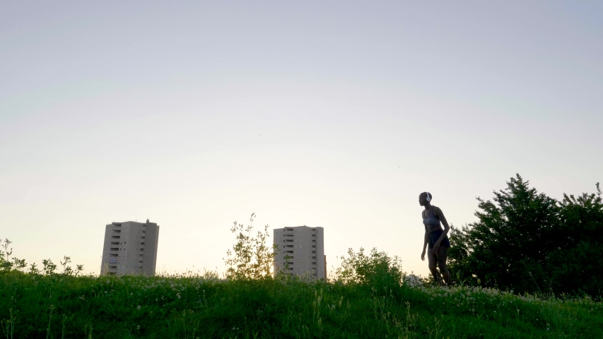 Slow motion shot of woman with headphones jogging on meadow at sunset