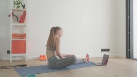 Healthy woman in sportswear at home stretching on yoga mat is using a laptop for the workout - sport recreation technology concept