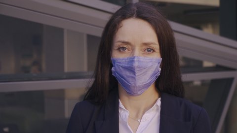 A young woman doing business wears a medical face mask to avoid the spread of coronavirus in the street. A close-up steadycam shoot of a lady with a surgical mask on the face against COVID-19.