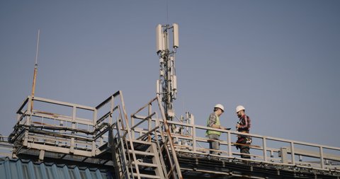 Wide shot of engineers talking while working on a cellular tower
