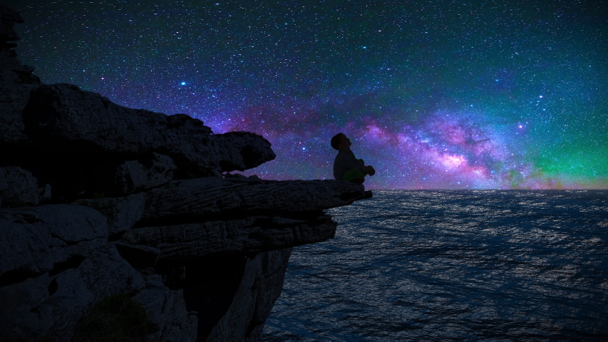The silhouette of a boy sitting on a cliff edge watching the milky way and shooting stars.