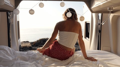 Female relaxing in van during vacation. Young woman travelling inside a camper van enjoys coastal views from her home. Alternative living  : vidéo de stock