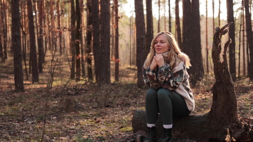 Young and beautiful blonde woman sitting on the log in the autumn forest, lighted with sun rays