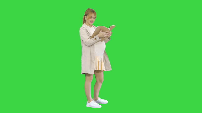 The pregnant woman standing with a book on a Green Screen, Chroma Key.