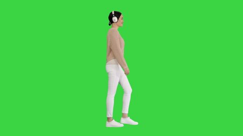Young woman with headphones walking listening to the music on a Green Screen, Chroma Key.