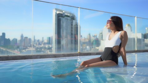 Beautiful Asian Woman Sitting in Rooftop Swimming Pool, City Skyline.