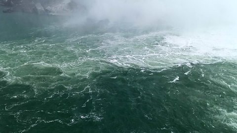 Slowmotion of green turquoise river water of Niagara falls with white steam in cold winter. Wavy water with white foam.