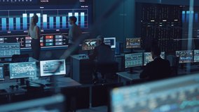 Two Software Engineers Talking Next to a Big Screen in a Modern Monitoring Office with Live Analysis Feed with Charts. Monitoring Room Big Data Scientists and Managers Sit in Front of Computers. - Powered by Shutterstock - Get 15% off with code: PIKWIZARD15