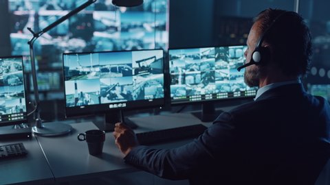 Male Officer Works on a Computer with Surveillance CCTV Video Footage in a Harbour Monitoring Center with Multiple Cameras on a Big Digital Screen. Employees Sit in Front of Displays with Big Data.