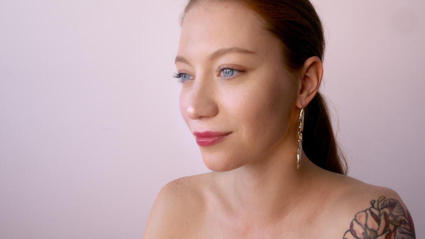 Beauty female tattooed model with red hair style and trendy beautiful makeup holding pink sweet colorful lollipop candy.Fashion woman having fun over background