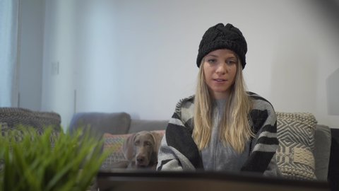 A joyful woman doing a video call while sitting with her dog and drinking coffee