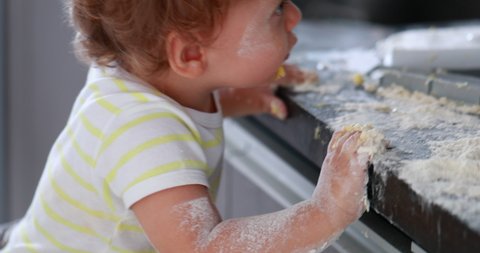 Messy baby child covered with flour at kitchen. Infant one year old toddler boy playing at kitchen.
