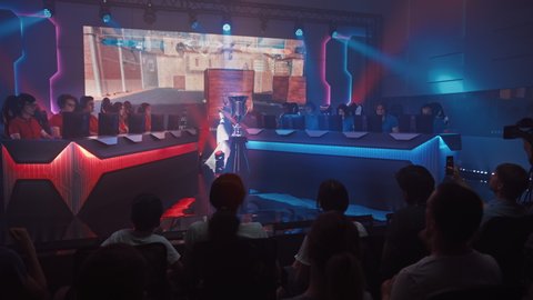 Two Esport Teams of Pro Gamers Play in FPS Shooter Video Game on a Championship Arena, Happy Team Wins Round and Celebrates with High-Fives.Big Screen Showing Mock-up Gameplay. Cyber Games Tournament 