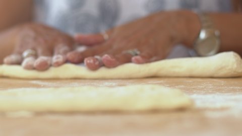 Front shot of woman making homemade pasta or breadsticks. Close up on hands kneading the dough and making potato gnocchi rolling the dough piece on the floured surface into a rope.