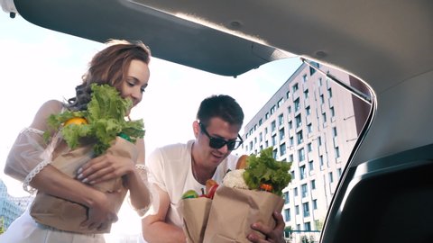 Young Joyful Couple Together Unloads, Closes Car Trunk, Carries Food Packages After Shopping in Grocery Store. Funny Purchases, Real Happy Relationship, Modern Lifestyle of Two Excited Friends Outdoor