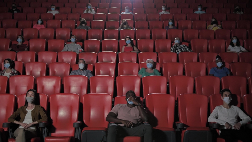 Multinational audience in face masks social distancing in movie theater during covid19 epidemic. Multi-ethnic viewers in face masks enjoying film despite the threat of coronavirus infection | Shutterstock HD Video #1056911579