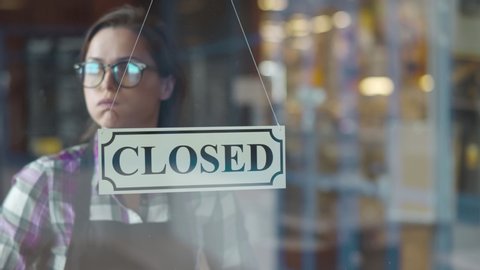 Young tired waitress turning sign to closed on cafe glass door at end of working day. Exhausted coffee shop owner closing place turning sign in evening. Small business development concept
