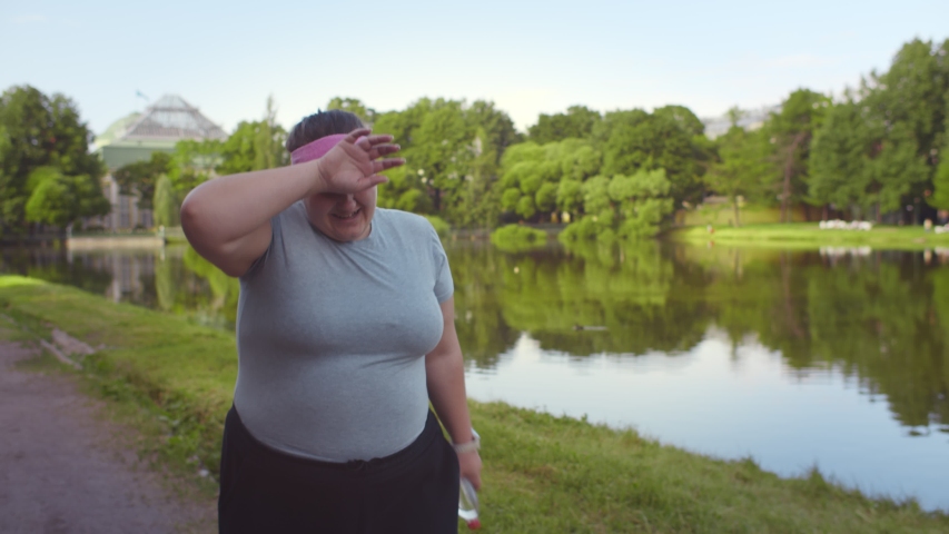 Obese woman feeling tired while running in summer park. Exhausted plus size young female slowly jogging outdoors during workout. Weight loss and healthy lifestyle concept Royalty-Free Stock Footage #1056912575
