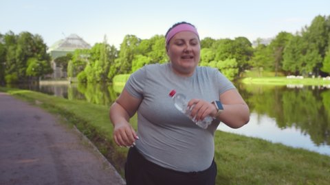 Obese woman feeling tired while running in summer park. Exhausted plus size young female slowly jogging outdoors during workout. Weight loss and healthy lifestyle concept