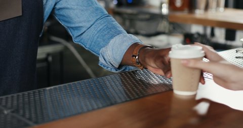Close up of hands of multiethnic bartender man and client woman. African American barrista handing coffee to Caucasian female. Mixed-races. Passing coffee-to-go at counter. Giving ordered drink. Order