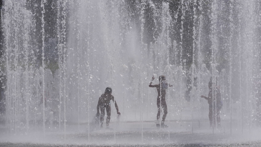 Silhouettes, Kids Having Fun Between Water Splash in Fountain on Street. Heat in Europe. Silhouettes Children Play in City Fountain on Hot Summer Day. Slow Motion. Global warming. Royalty-Free Stock Footage #1056916757