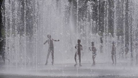 Silhouettes, Kids Having Fun Between Water Splash in Fountain on Street. Heat in Europe. Silhouettes Children Play in City Fountain on Hot Summer Day. Slow Motion. Global warming.