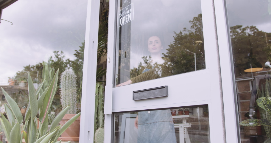 Small business entrepreneur female opening door of plant shop and looking outside for customer