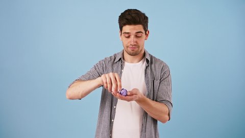Young man in casual outfit is holding bottle of medicine, takes one pill and smiling. Posing on blue background. Close up, copy space