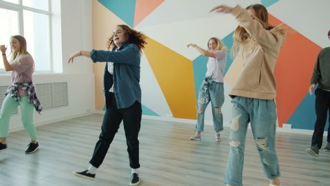 Cheerful men and women are dancing hip-hop dances in modern studio having fun together wearing trendy clothing. Dancers and contemporary art concept.