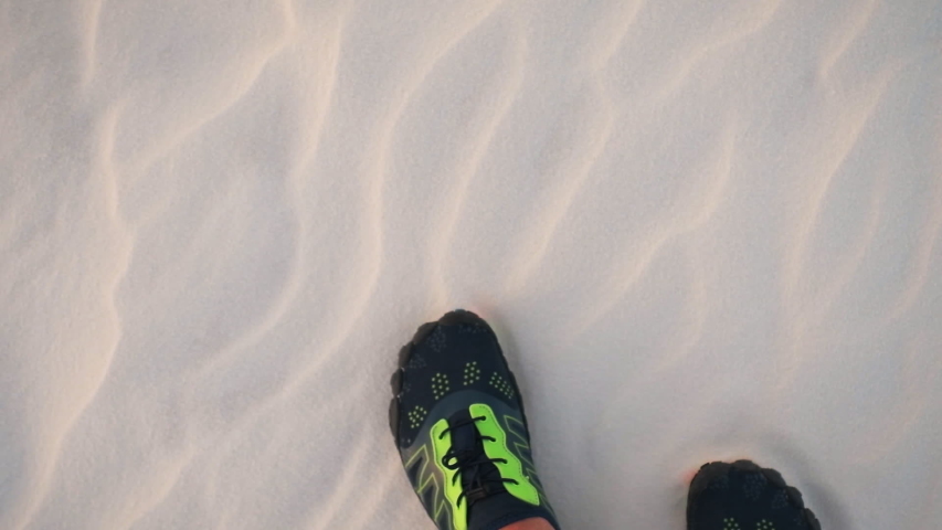 Point of view pov looking down of male legs and feet water shoes on sand in white sands dunes national monument in New Mexico showing texture walking on surface in slow motion