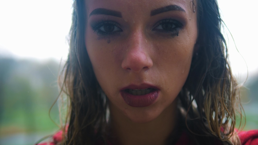 Young beautiful woman stands in the rain and looks at the camera