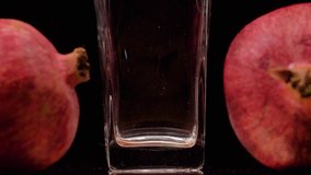 Premium Taste. Slow motion shot of pouring pomegranate juice into a transparent glass and two pomegranates against black background. Filling glass with pomegranate juice close up 4K video